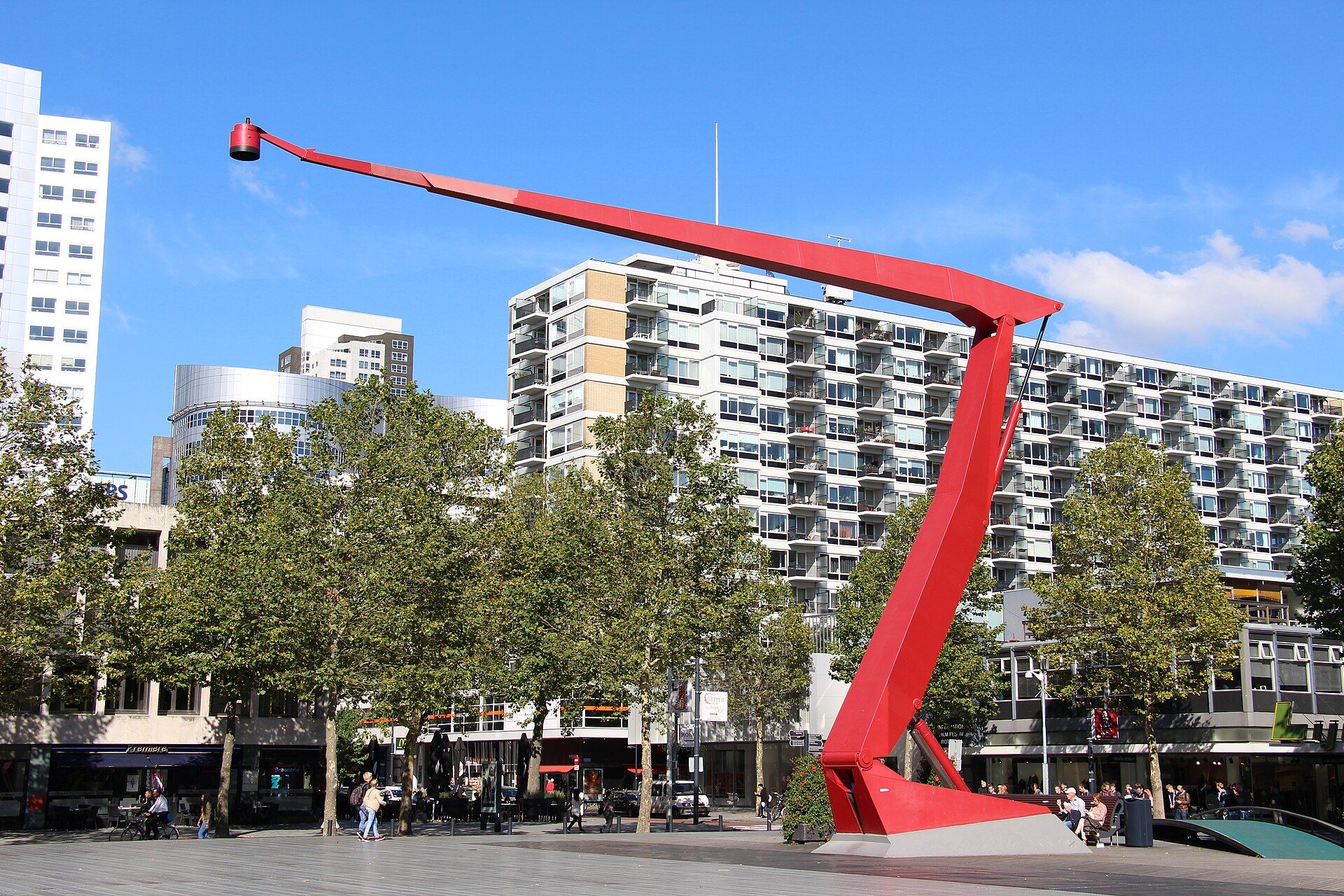 One of the tall red lamps on Schouwburgplein, with trees and blocks of flats behind it.